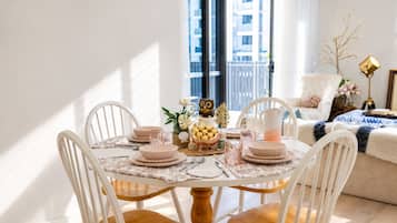 A dining area with a round table, white chairs, and a view of a building through a window.