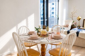 A dining area with a round table, white chairs, and a view of a building through a window.