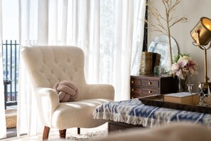 A room with a tufted armchair, a small side table, a lamp, and a mirror on a dresser.