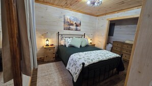 A cozy bedroom with a wooden ceiling, a bed with green bedding, two bedside tables with lamps, a nightstand, and a wooden dresser. - Nice 2-bedroom cottage with AC in Mountain View (Mountain View)
