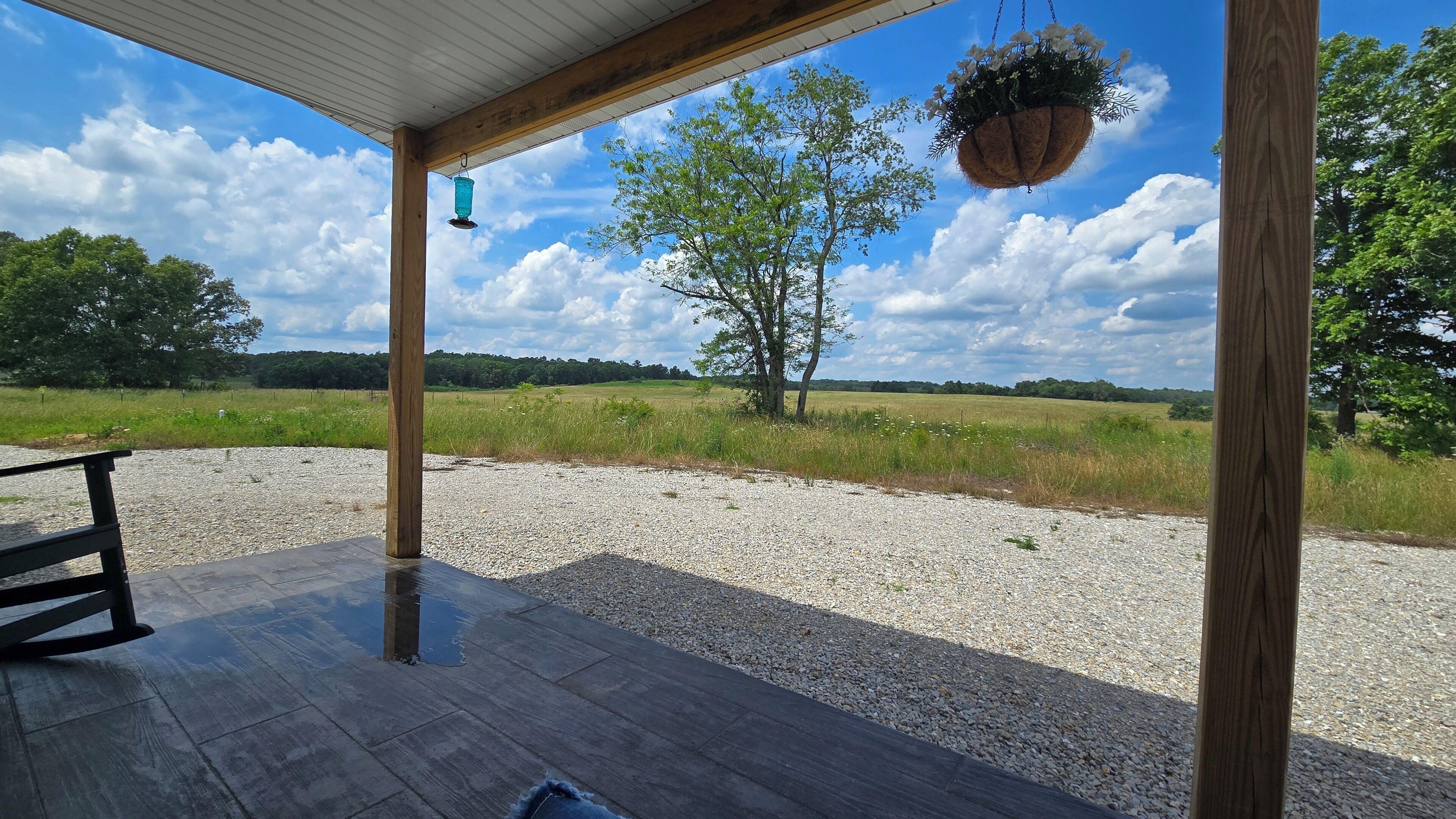 An outdoor wooden deck with a gravel path, a hanging flower basket, and a bench.