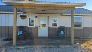 A covered porch with two wooden chairs and a hanging flower basket. - Nice 2-bedroom cottage with AC in Mountain View (Mountain View)