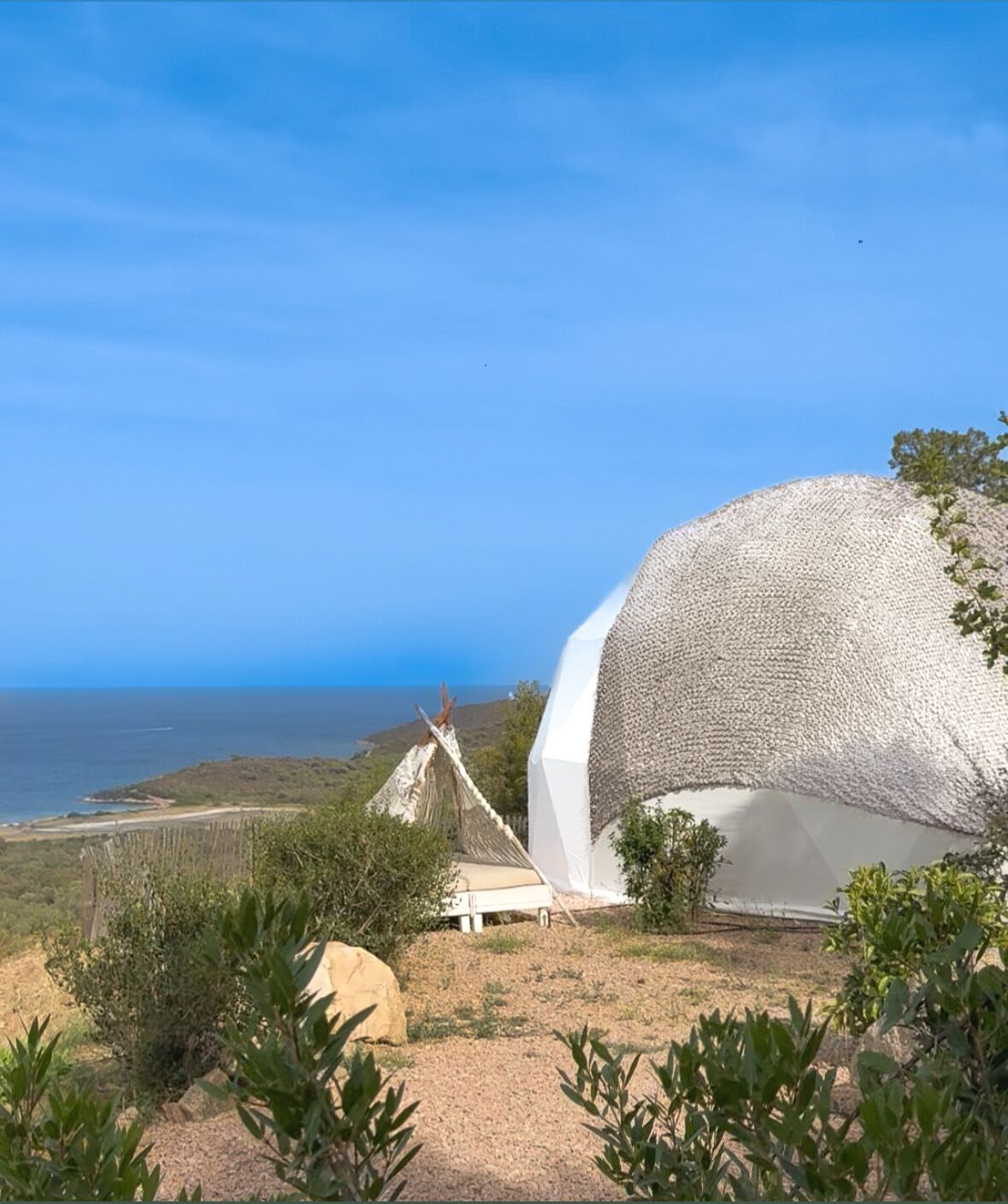 Un edificio de forma abovedada, blanco, con un exterior de fibras naturales trenzadas, ubicado en un paisaje costero con vista despejada al mar.