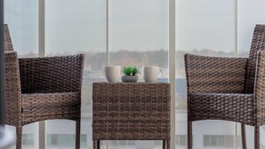 Two wicker chairs, a small table with a plant and two white cups, and a window with a mesh screen. - Spacious Apartment | Balcony and Private Parking in Garage (Łódź)