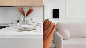 A modern kitchen with white cabinets, a marble countertop, and a dining area with white plates and glasses. - Spacious Apartment | Balcony and Private Parking in Garage (Łódź)