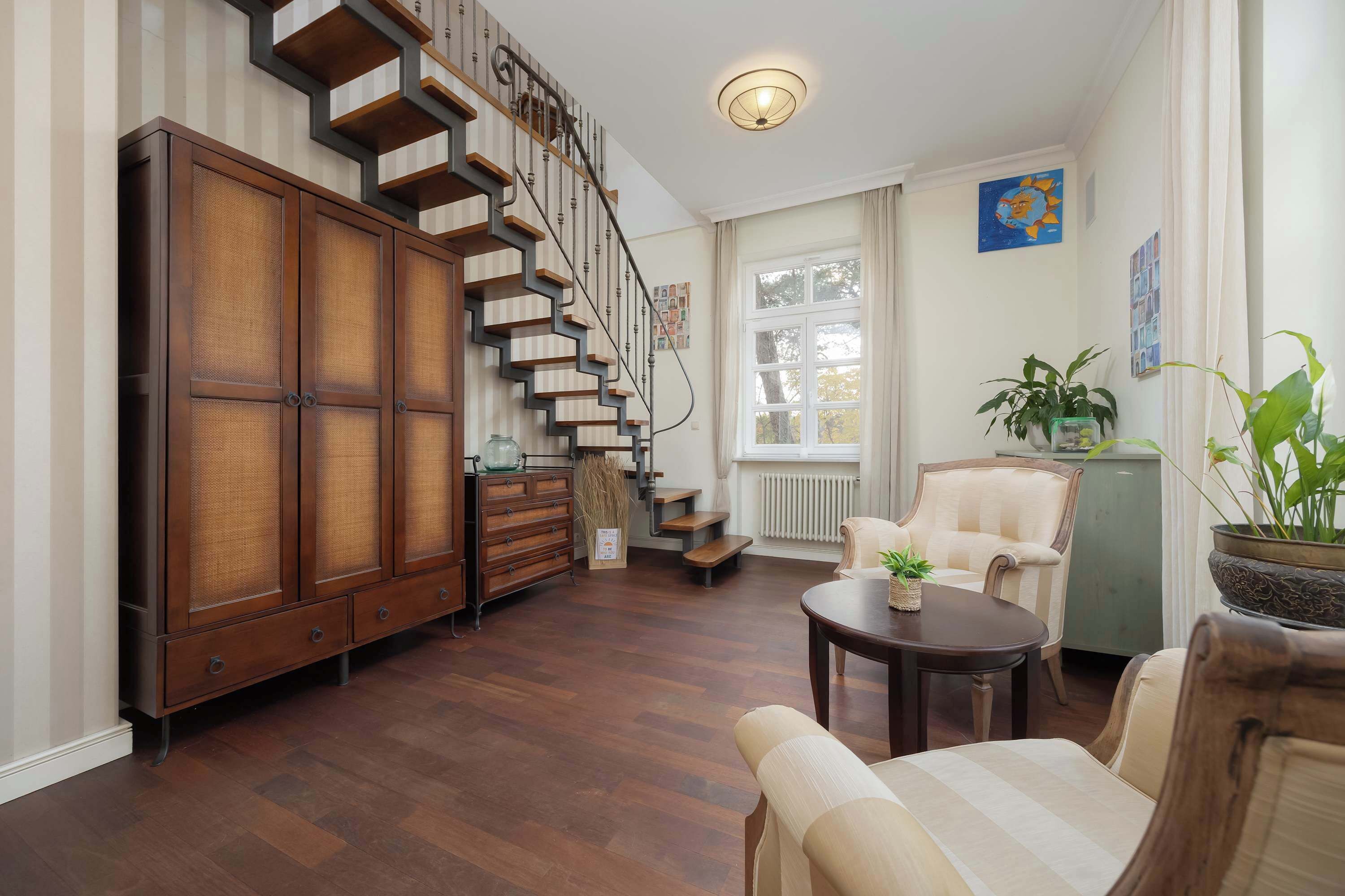 Un salón espacioso con escalera de madera, zona de comedor y un ventanal que proporciona luz natural.
