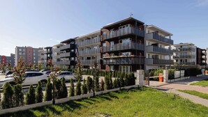 Un immeuble résidentiel moderne à plusieurs étages, doté de balcons, d’un espace de stationnement et d’une pelouse bien entretenue.