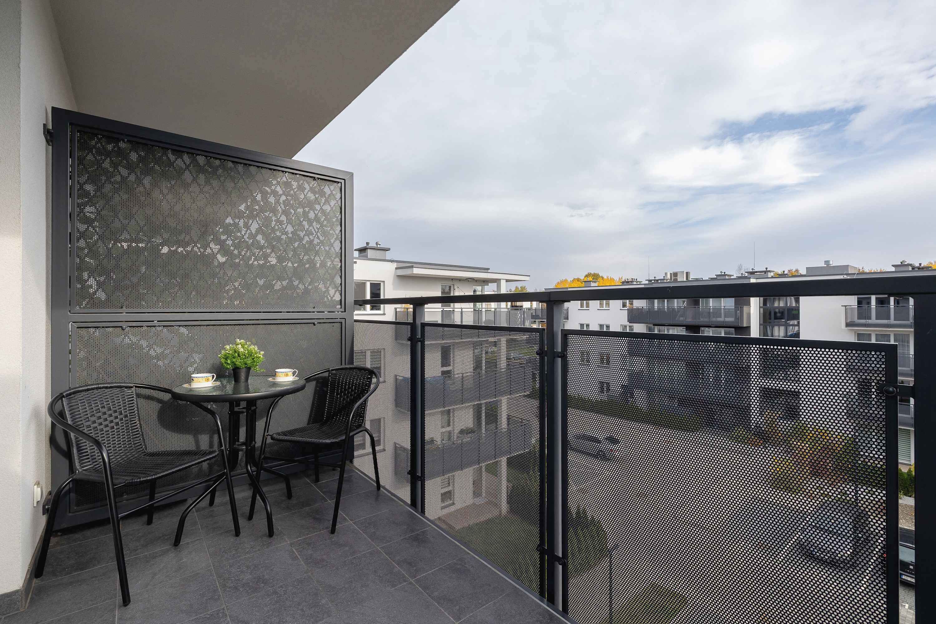 Un balcón con mesa y sillas, una planta en maceta y vistas de la ciudad.