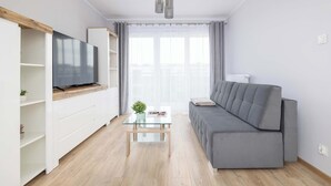 Un salon moderne avec un canapé gris, une table basse en verre et un téléviseur posé sur une étagère en bois.