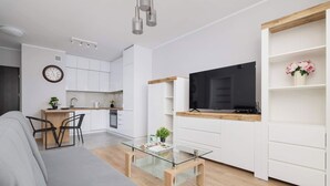 Un salon moderne avec une table basse en verre, un canapé et un téléviseur posé sur une étagère en bois.
