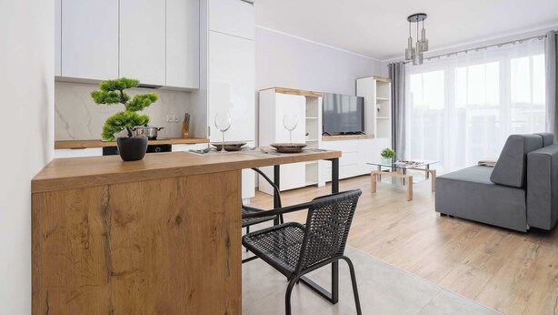 Une cuisine moderne avec des meubles blancs, un îlot central en bois et un coin repas agrémenté d’une chaise noire.
