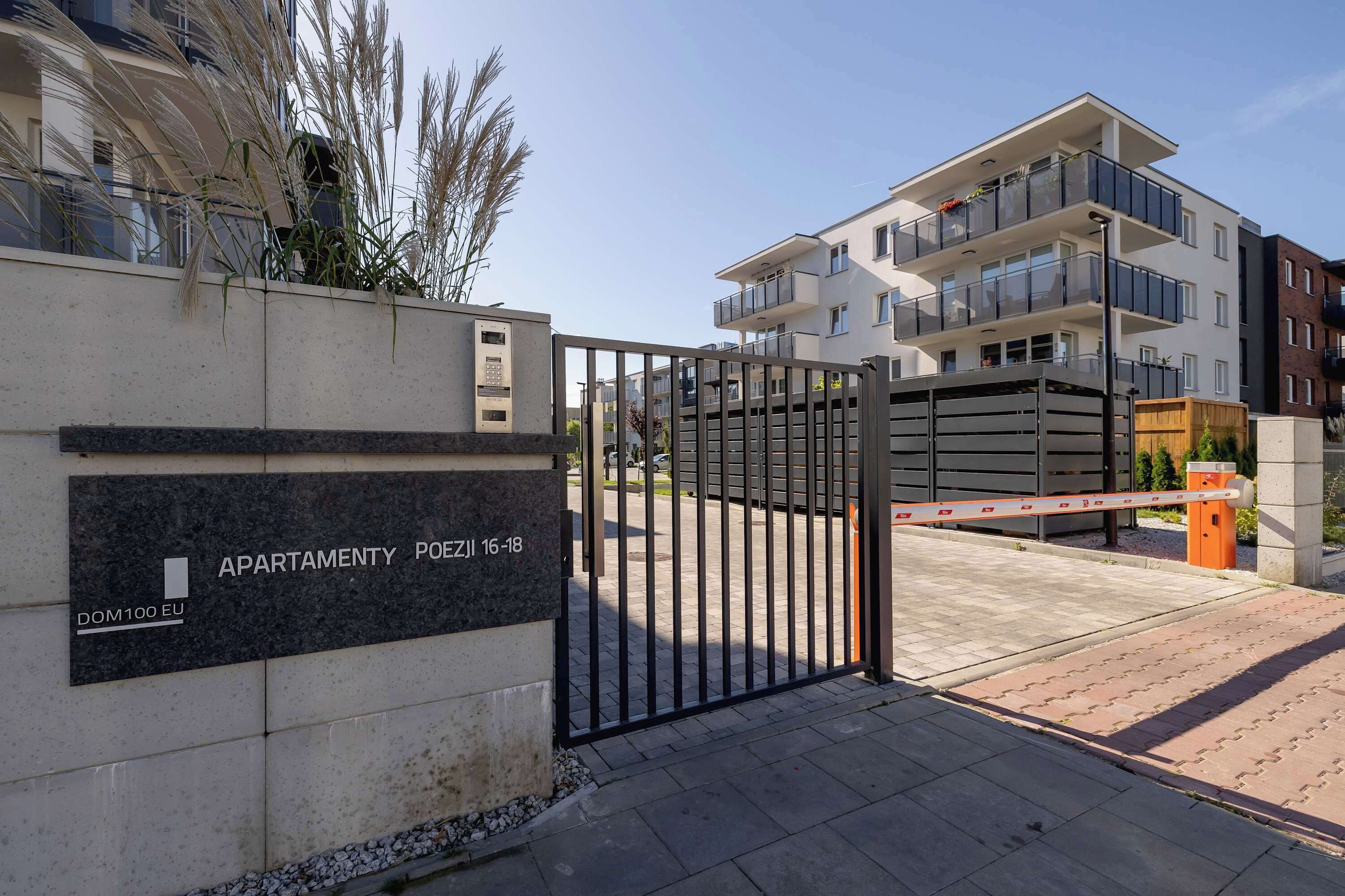 Una entrada cerrada a un complejo de apartamentos con un letrero que indica 'APARTMENTY POEZIL 16-18' y 'DOM100 EU'.