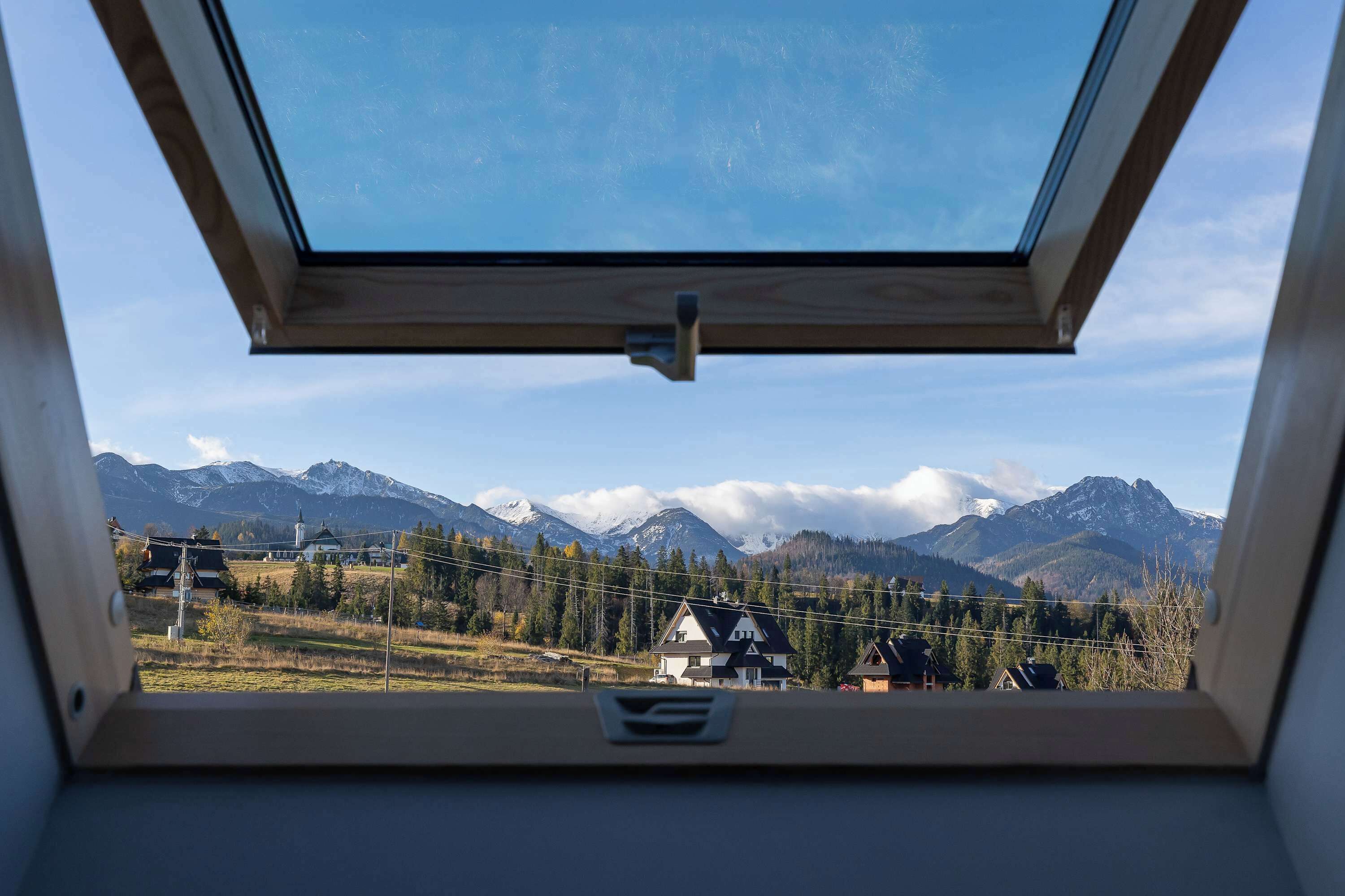 A view through a skylight of a mountainous landscape with snow-capped peaks and a clear sky.