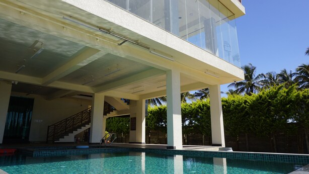 A modern building with a swimming pool, large windows, and a staircase leading to an upper level. - AT CKM Homestay (Chikkamagaluru)