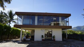 A modern building with a glass facade, a wooden upper section, and a sign indicating a contact email. - AT CKM Homestay (Chikkamagaluru)