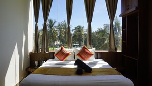 A hotel room with a bed, curtains, and a view of palm trees. - AT CKM Homestay (Chikkamagaluru)
