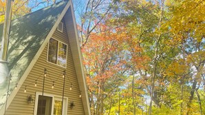 Une cabane dotée d’une terrasse en bois et d’une cheminée, entourée du feuillage automnal.