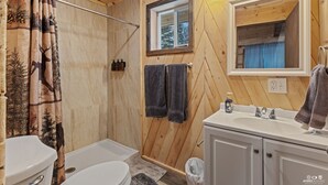 Baño de cabaña de madera con inodoro, ducha, lavabo y ventana.