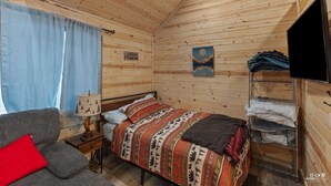 Una habitación tipo cabaña acogedora con una cama, un sofá, una lámpara y un televisor.