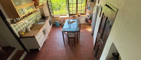 A compact kitchen with a dining area, a window with a view of greenery, and a tiled backsplash.