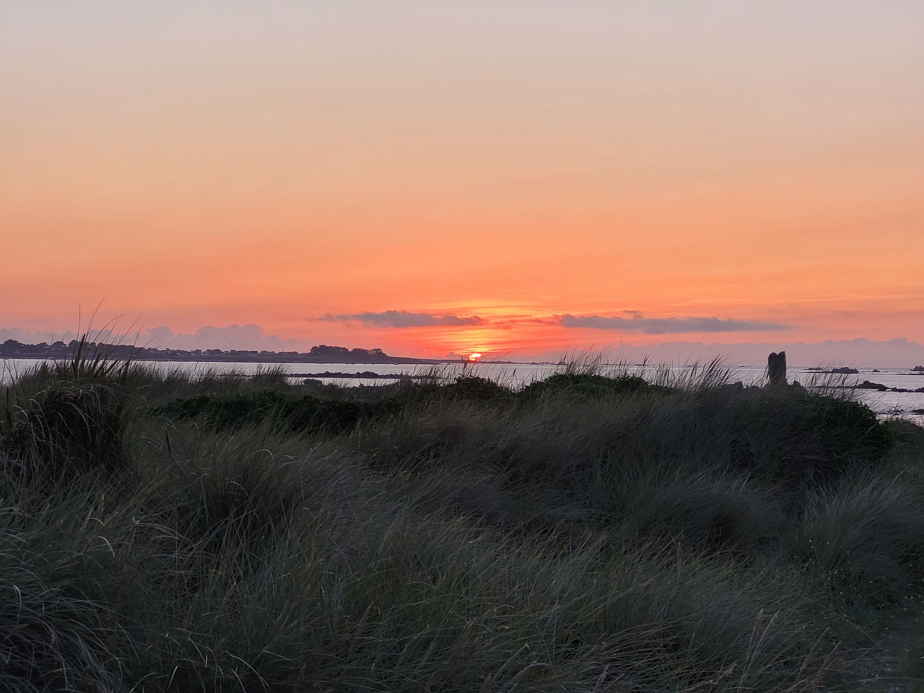A sunset over a coastal landscape with grassy dunes in the foreground.