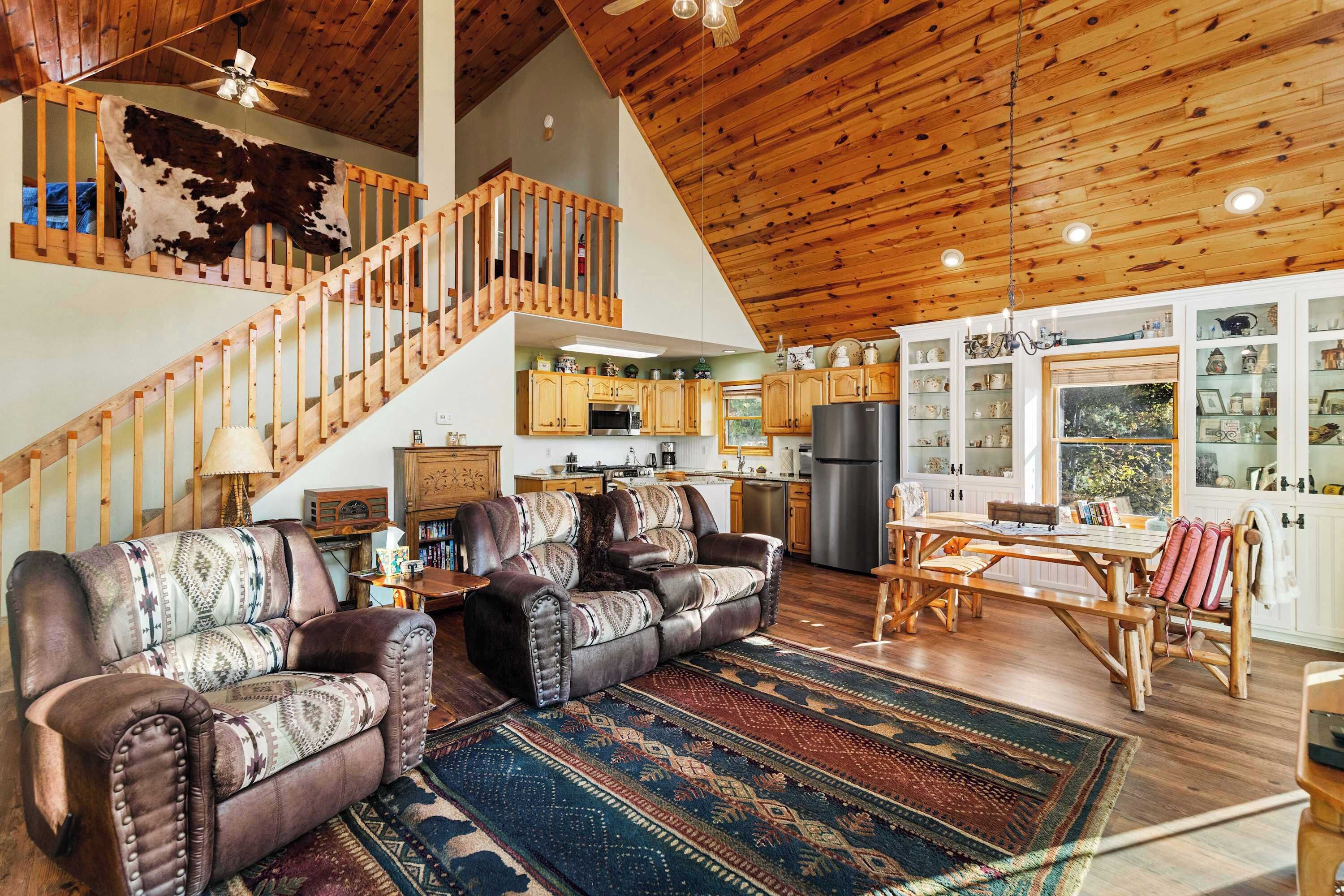 A spacious living area with leather sofas, a wooden staircase, and a kitchen in the background.