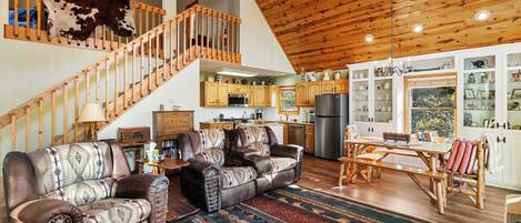 A spacious living area with leather sofas, a wooden staircase, and a kitchen in the background.