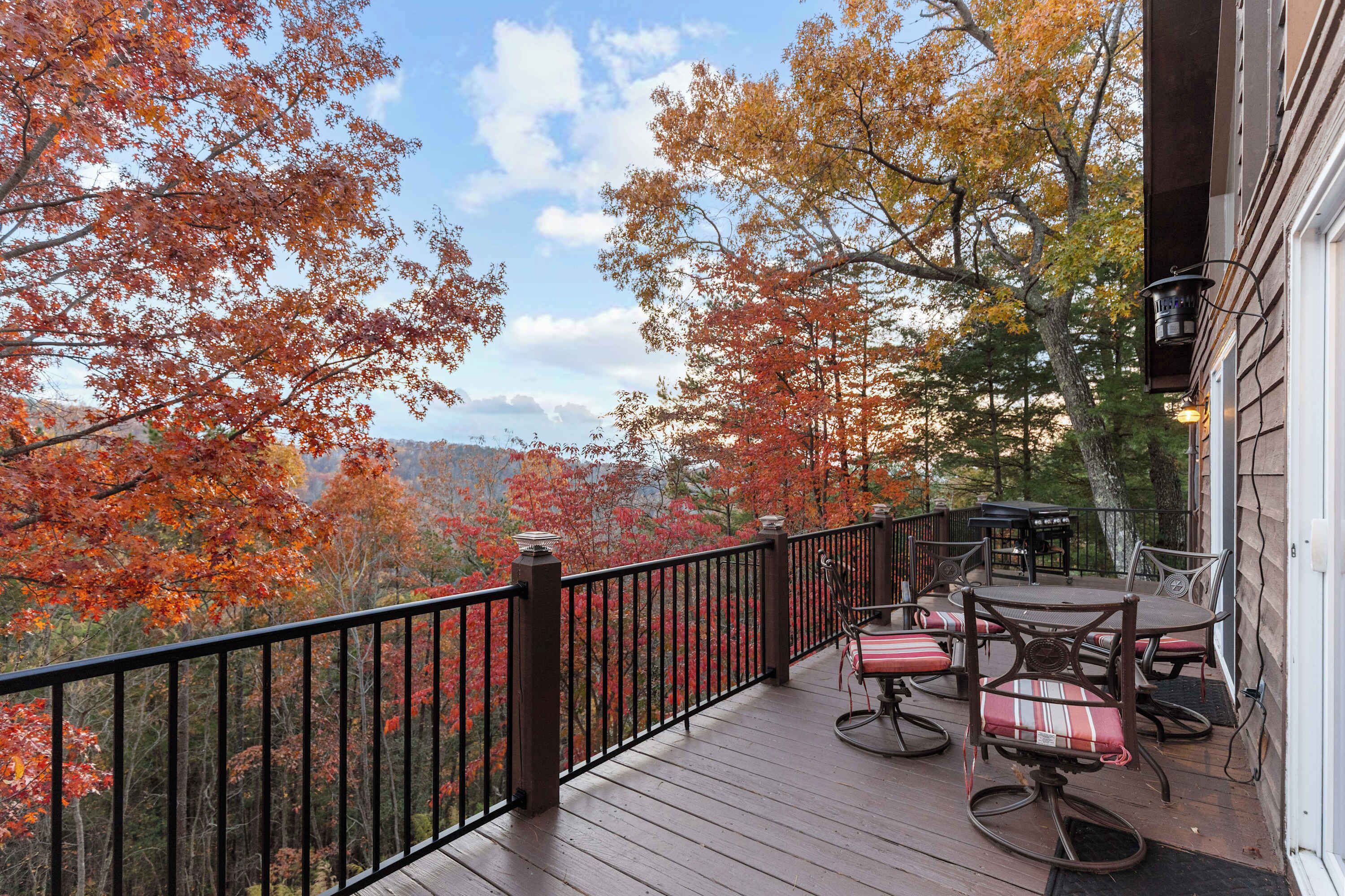 Une terrasse en bois, dotée de mobilier d’extérieur, d’une rambarde et offrant une vue sur des arbres aux feuilles d’automne.