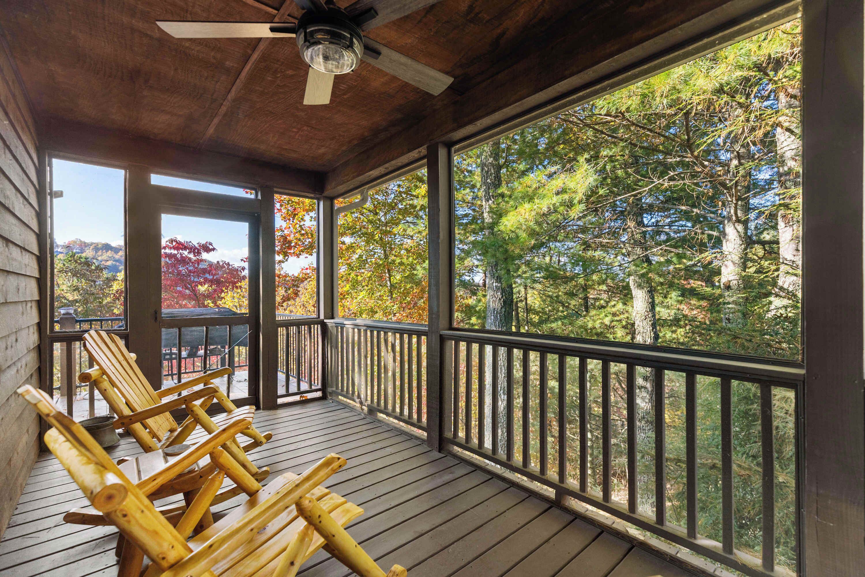 Une terrasse en bois avec un ventilateur de plafond, des chaises en bois et une vue sur les arbres.