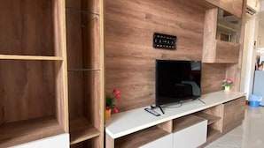 A modern living room with a wooden entertainment unit, a flat-screen TV, and a small table with a vase of flowers. - Aksarai Hotel Patong  (Patong)