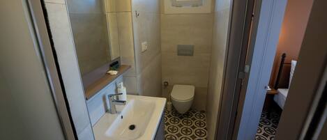 Un baño pequeño con un lavabo blanco, un inodoro y un ventanal.