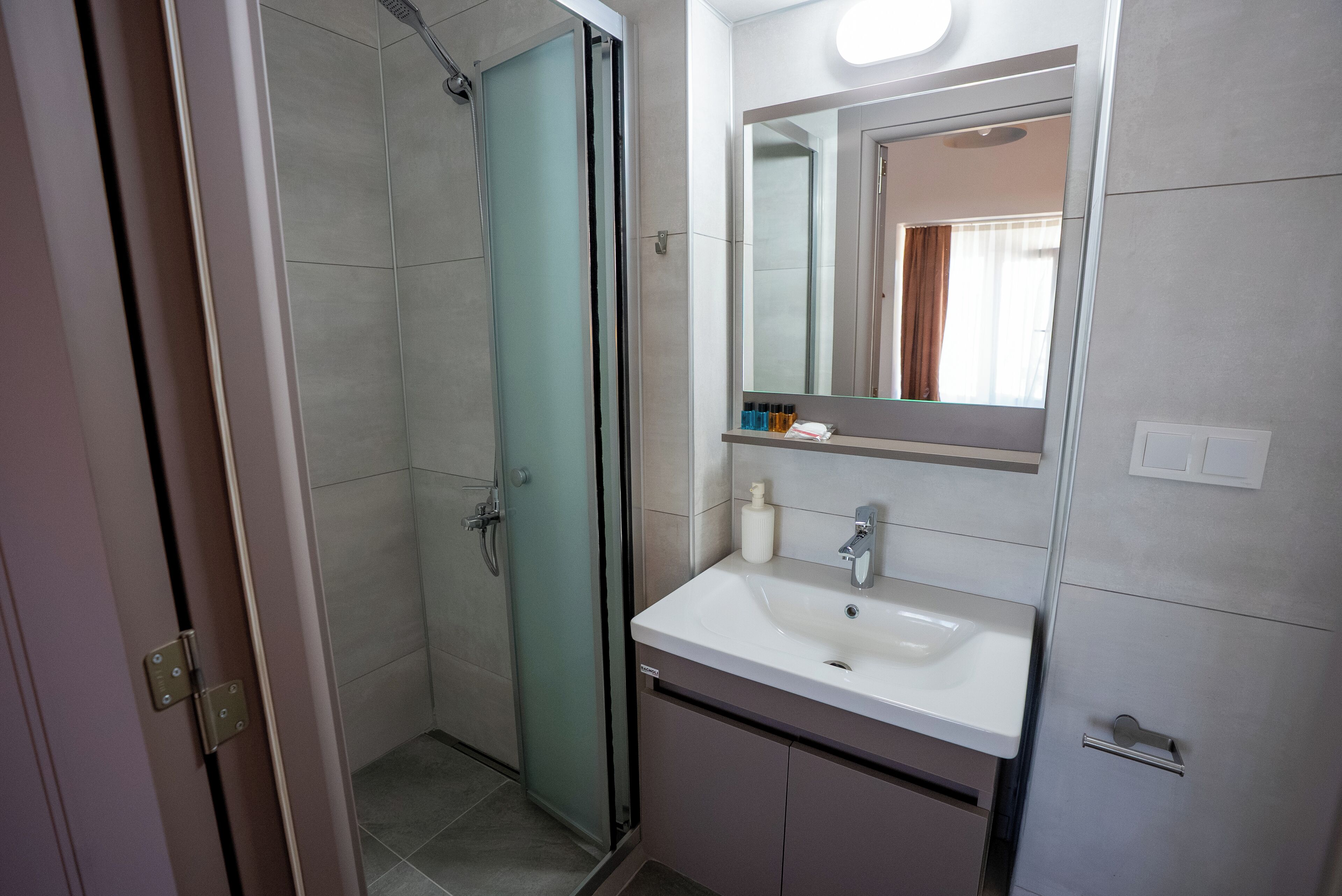 Een moderne badkamer met een douchecabine van glas, een witte wastafel en een grote spiegel erboven.