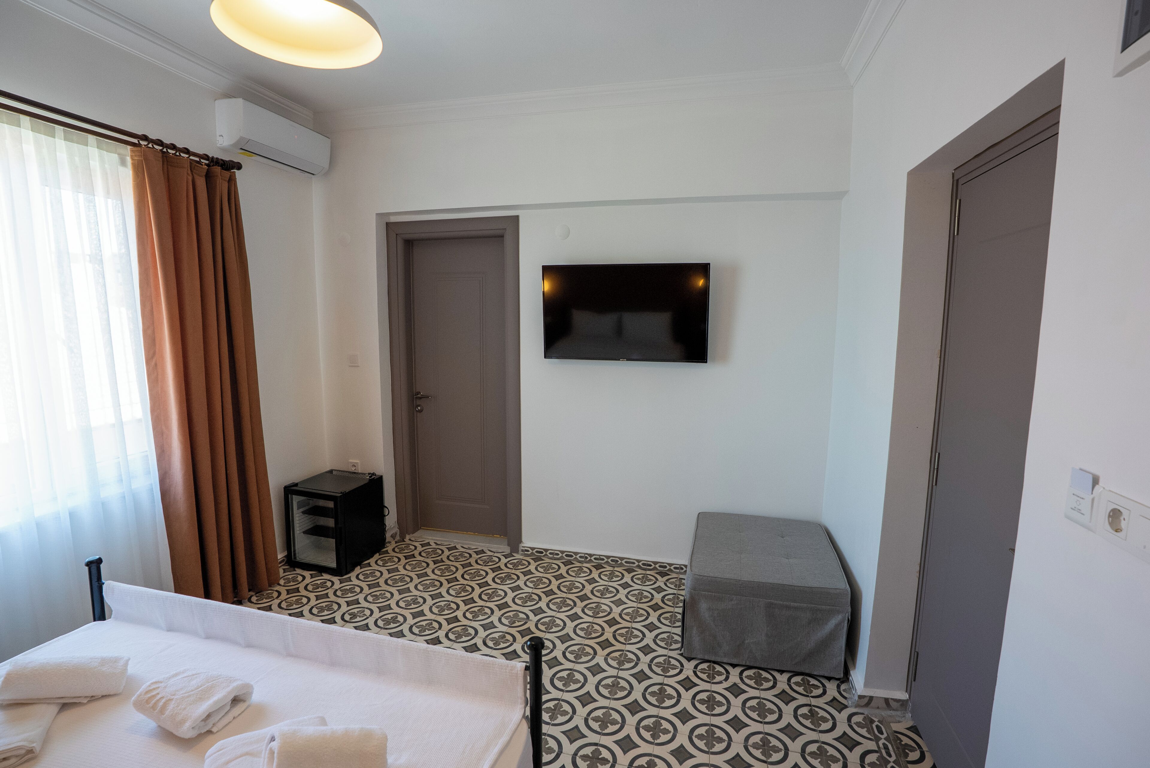 Een hotelkamer met een bed, een televisie, een deur en vloerbedekking met een patroon.
