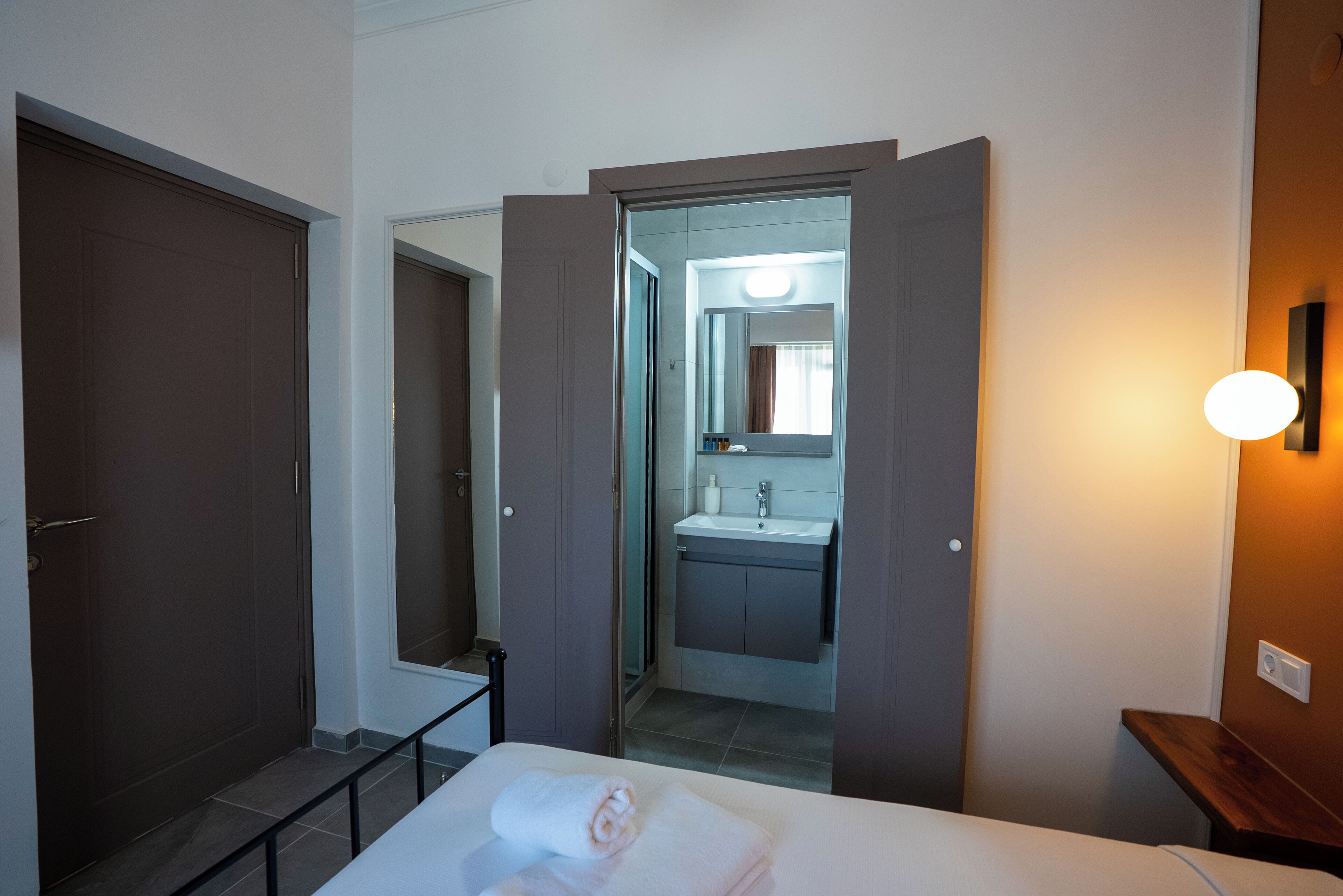 Una habitación de hotel con cama, un baño con lavamanos y espejo, y una puerta que da a otra habitación.