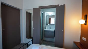 Una habitación de hotel con cama, un baño con lavamanos y espejo, y una puerta que da a otra habitación.