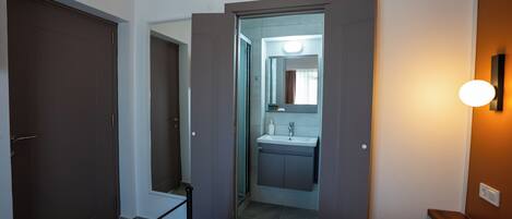 A hotel room with a bed, a bathroom with a sink and mirror, and a door leading to another room.