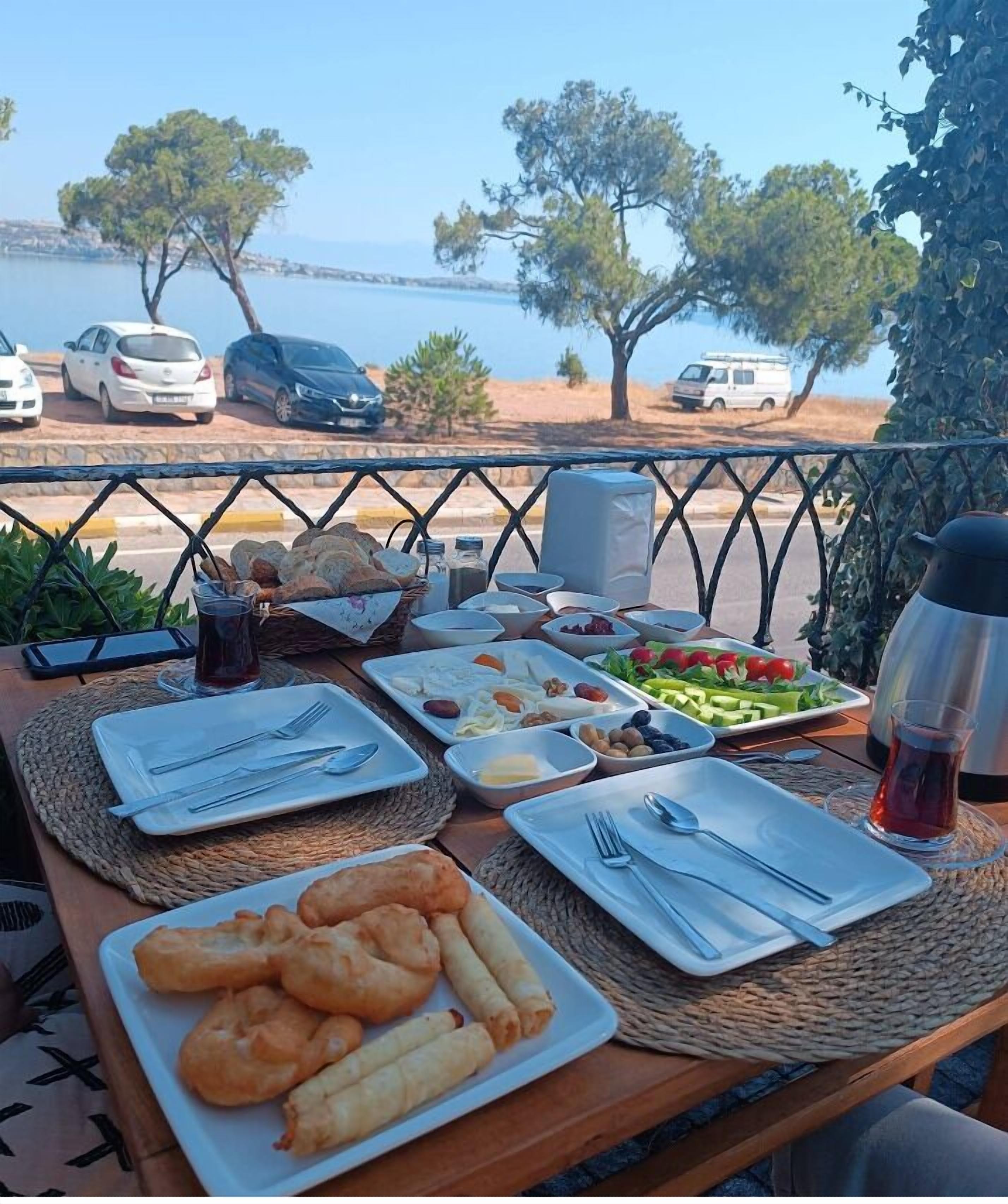A table set with various dishes and drinks, overlooking a scenic view of the sea and parked cars.