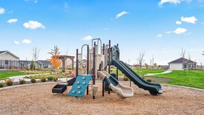 Un terrain de jeux équipé d’un toboggan et de structures d’escalade, entouré d’un espace paysager avec de la pelouse et des arbres.