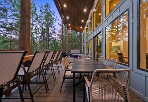 An outdoor dining area with a long table and chairs, surrounded by glass walls and wooden beams. - Ping-Pong Table | Corn Hole | EV Charger | Hot Tub (Broken Bow)