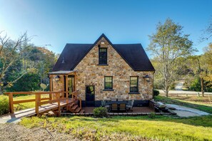 Una casa de piedra con una terraza de madera, un espacio de estar techado al aire libre y una pequeña escalera que conduce a la entrada.