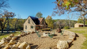 A stone house with a sloped roof, surrounded by a landscaped area with rocks and a fire pit. - Old Stone Cottage Retreat in the Heart of Missouri (Bourbon)