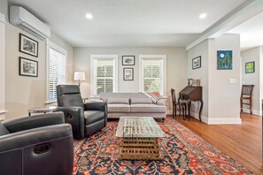 Un salon avec un canapé gris, des fauteuils en cuir noir, une table basse en bois et un tapis à motifs.