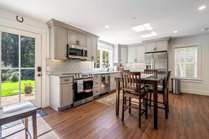 A modern kitchen with white cabinets, stainless steel appliances, and a dining area with wooden chairs.