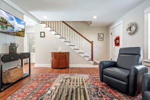 A living room with a wooden floor, a black leather chair, a patterned rug, a wooden cabinet, and a staircase.