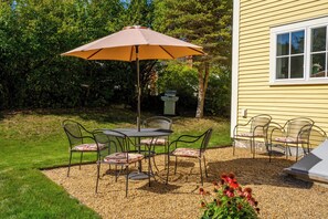An outdoor patio with a table and chairs, an umbrella, and a grill.