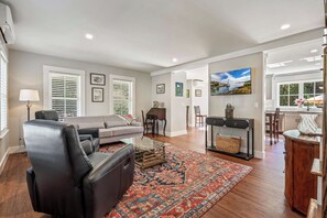 Un salon spacieux avec un canapé en cuir, une table basse et un tapis à motifs. On y trouve également un coin repas avec une table et des chaises, et une cuisine visible au fond.