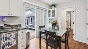 A modern kitchen with white cabinetry, a granite countertop, and a dining area with a glass table and dark wooden chairs. - Bay Ridge House- Charming 2-Bedroom Home – Large Backyard, Family-Friendly, Clos (Annapolis)
