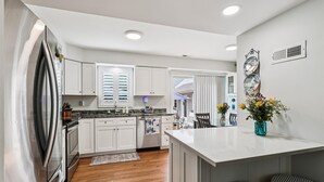 A modern kitchen with white cabinets, a stainless steel refrigerator, and a central island with stools. - Bay Ridge House- Charming 2-Bedroom Home – Large Backyard, Family-Friendly, Clos (Annapolis)