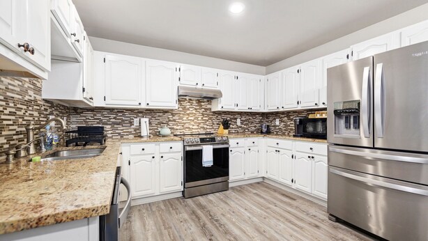 A modern kitchen with white cabinets, a stainless steel refrigerator, and a wood floor. - The Bentonville Basecamp (Bentonville)