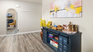 A modern living room with a wooden floor, a blue cabinet with decorative items, a large abstract painting, and a mirror reflecting a yellow chair and a painting. - The Bentonville Basecamp (Bentonville)